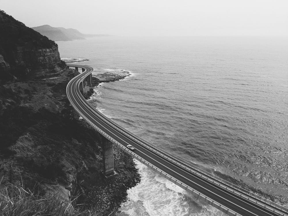Grayscale Photo of Road Near Body of Water