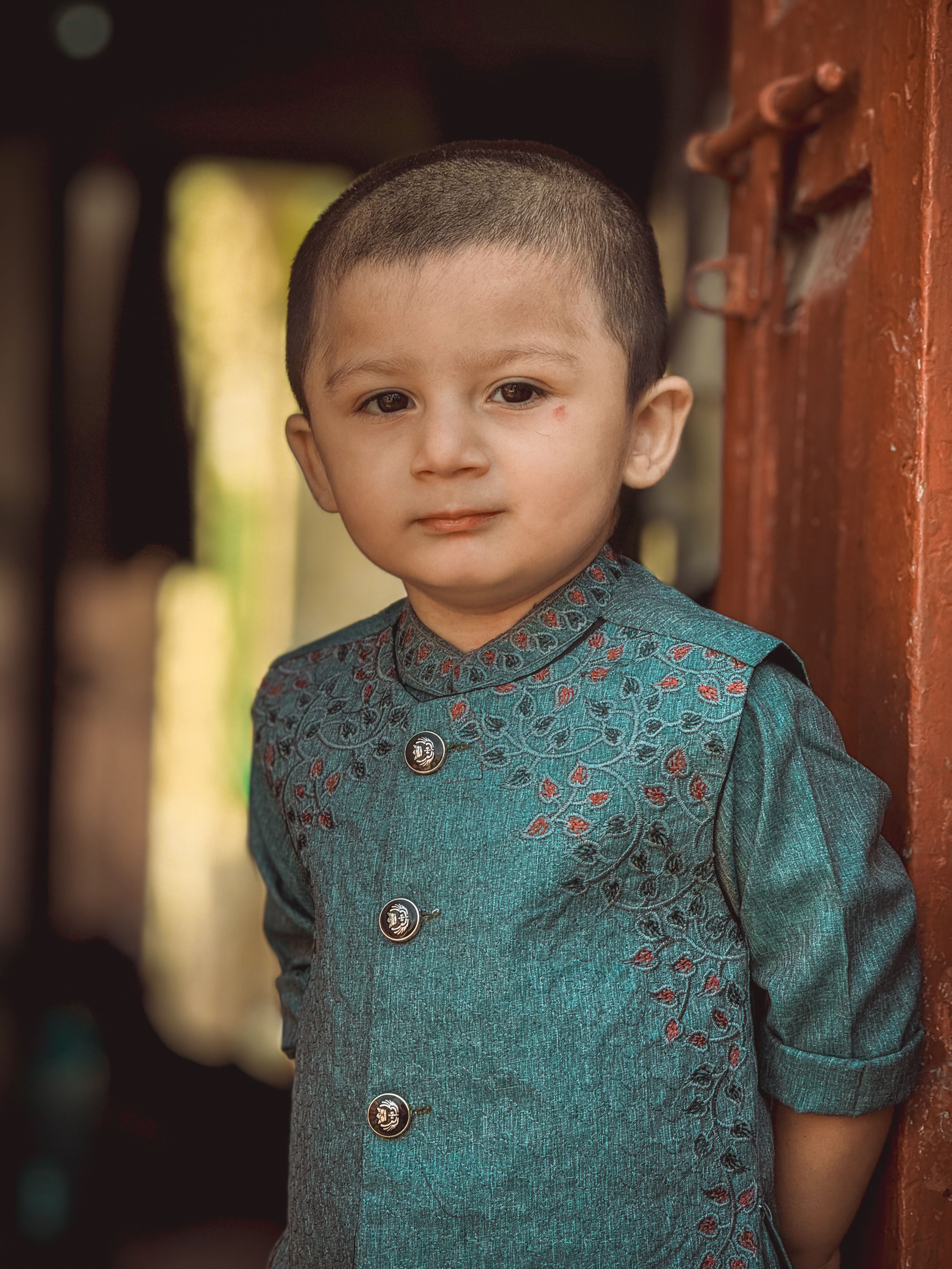 Charming portrait of a young boy in elegant turquoise traditional attire standing indoors.