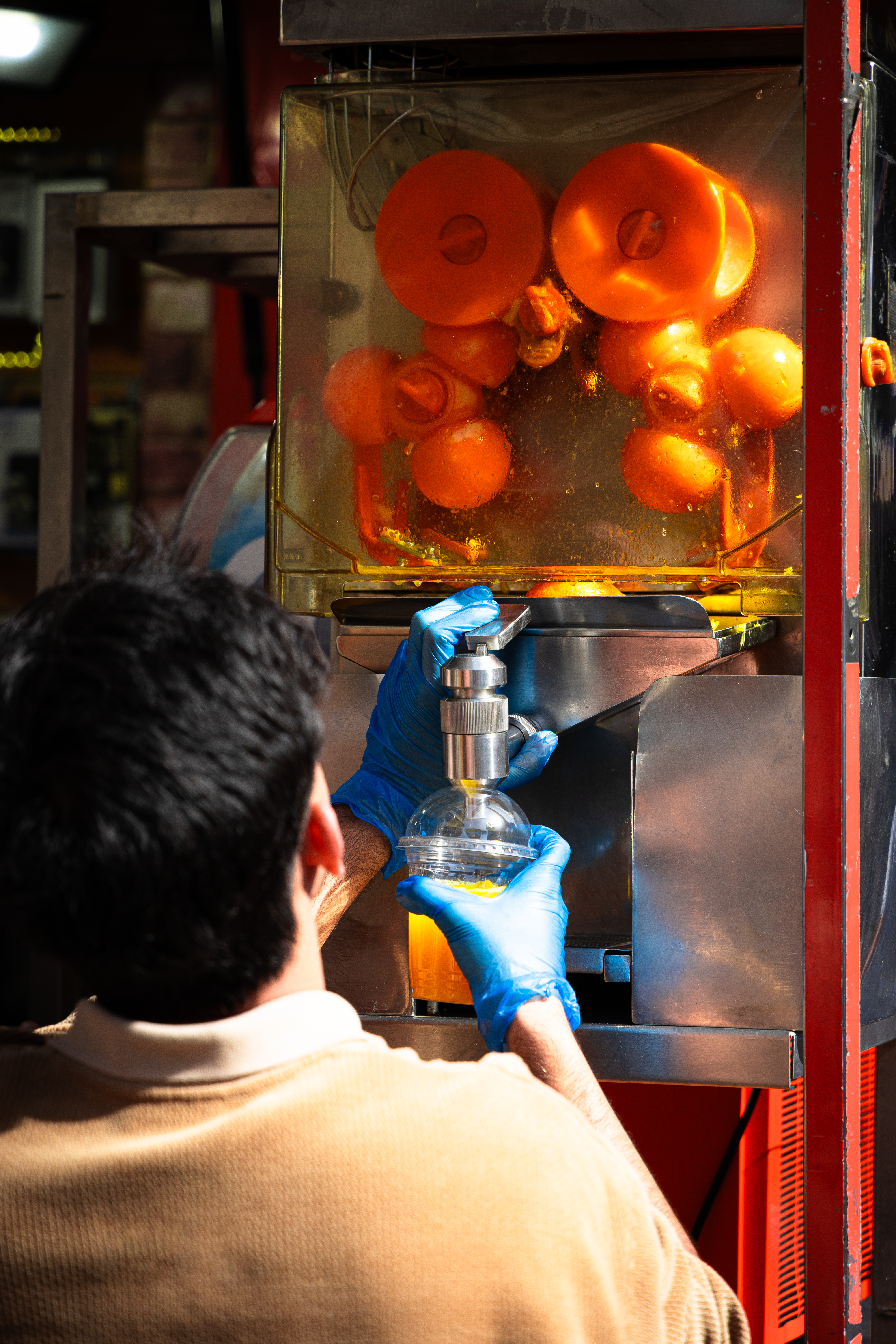 Vendor using a commercial orange juicer to prepare fresh juice at a market stall.