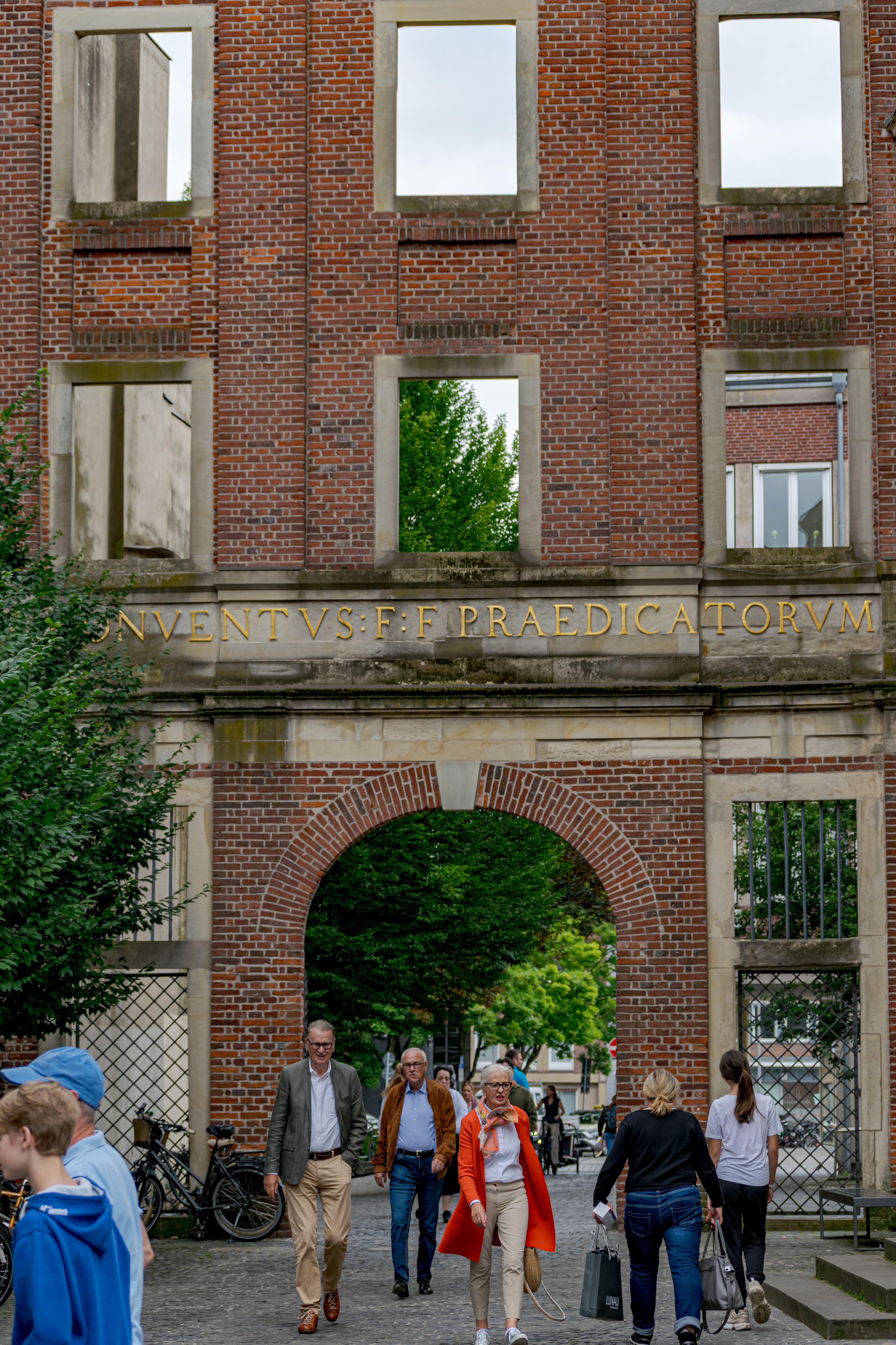 Crowd passing under an ancient brick archway in Münster, NRW, Germany.