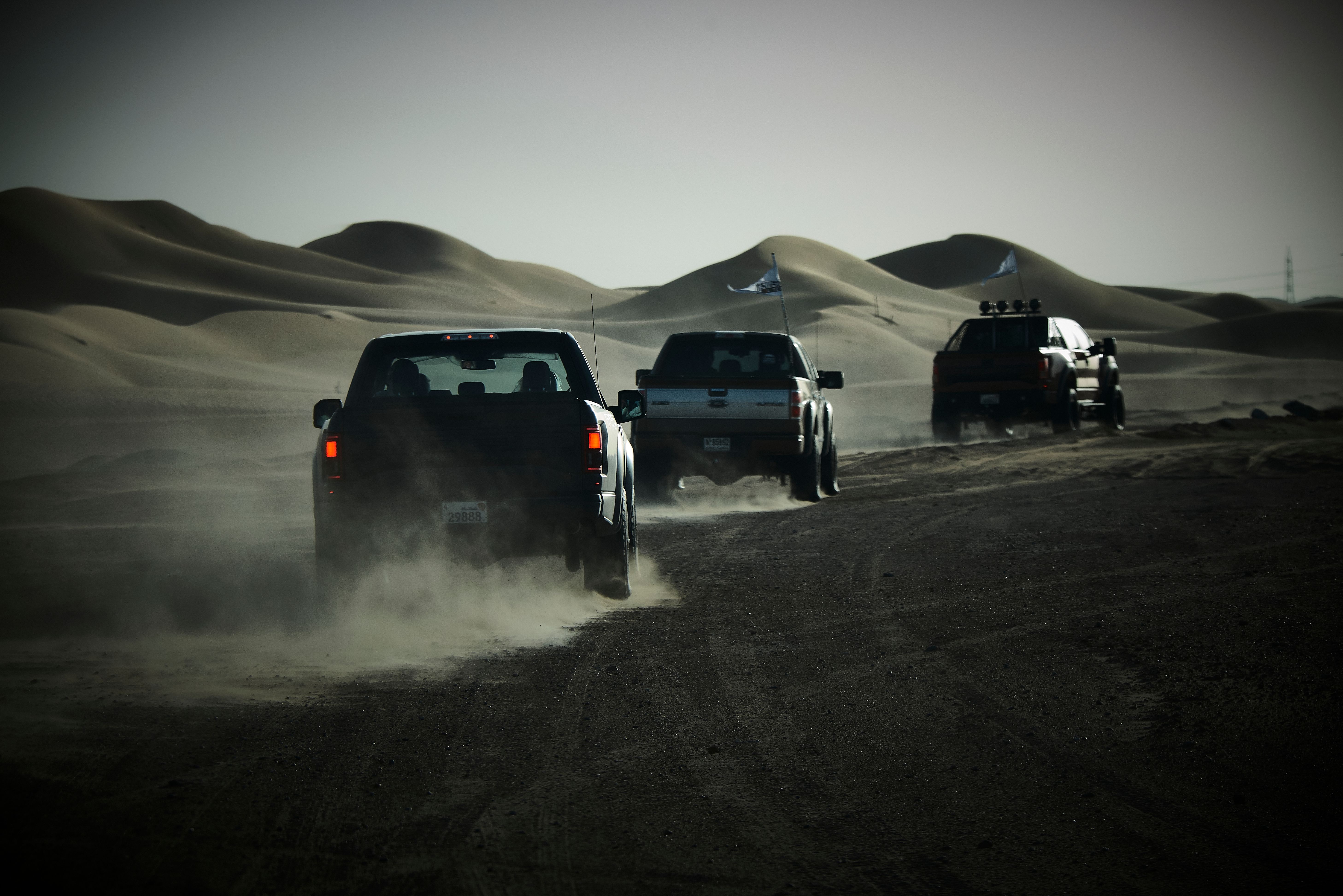 Three trucks traverse the scenic desert dunes of Dubai, capturing an off-road journey.