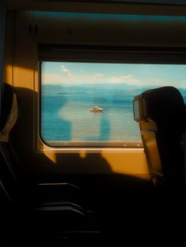 Peaceful view of a boat on calm waters through a train window, highlighting travel serenity.