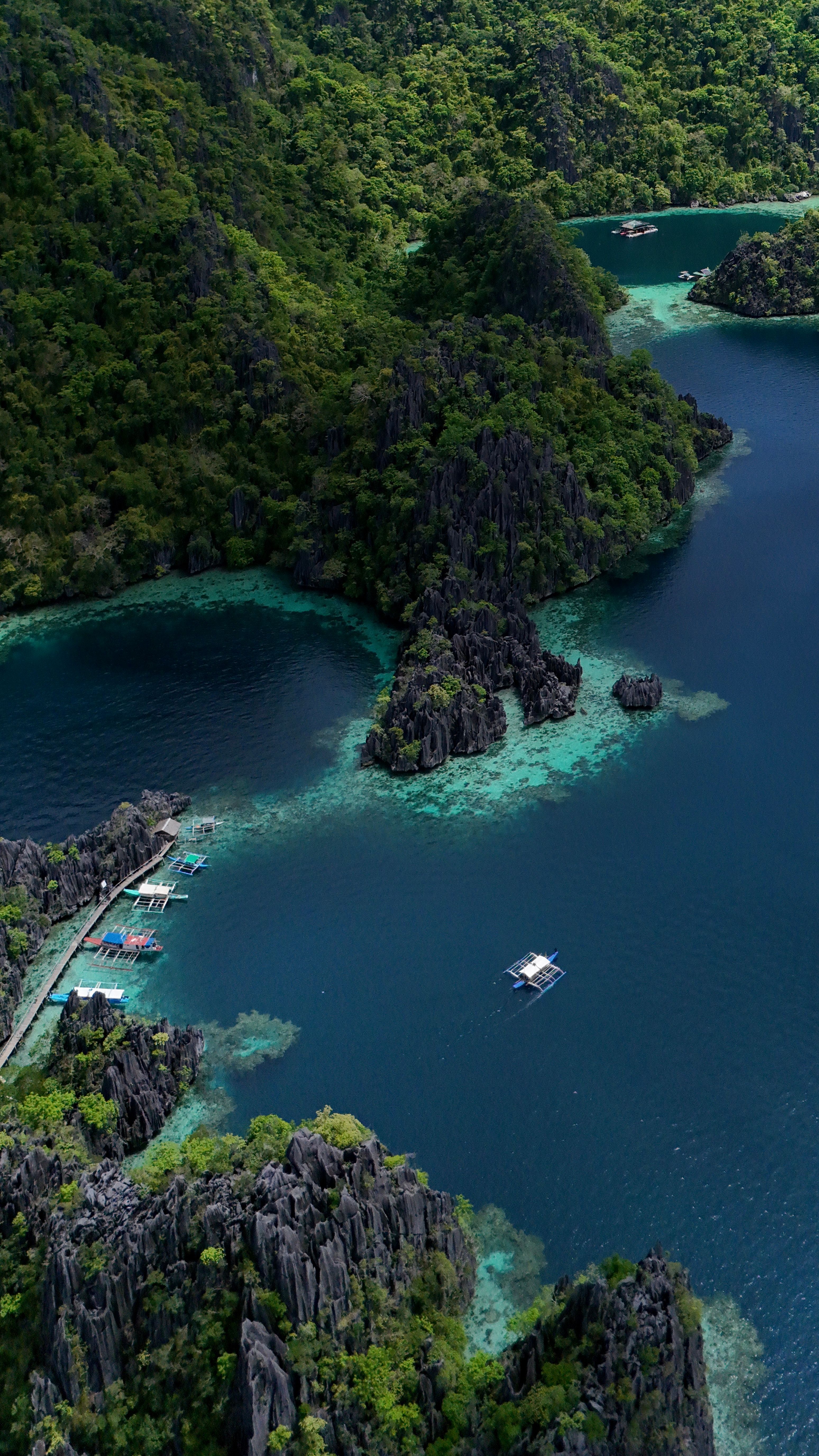 Aerial photo of boats in a clear blue lagoon surrounded by lush green vegetation and rocky hills.