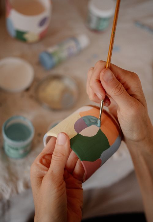 Free A close-up of hands painting colorful patterns on a ceramic pot, showcasing artistic creativity. Stock Photo