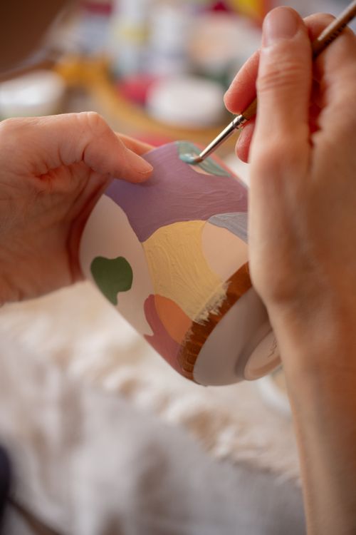 Free Close-up of hands painting a colorful ceramic pot with a fine brush. Stock Photo