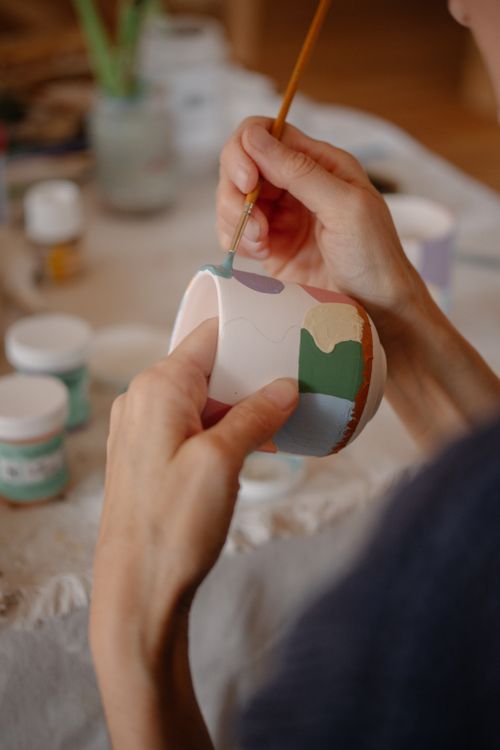 Free Close-up of hands painting a ceramic mug with colorful patterns in an artistic setting. Stock Photo
