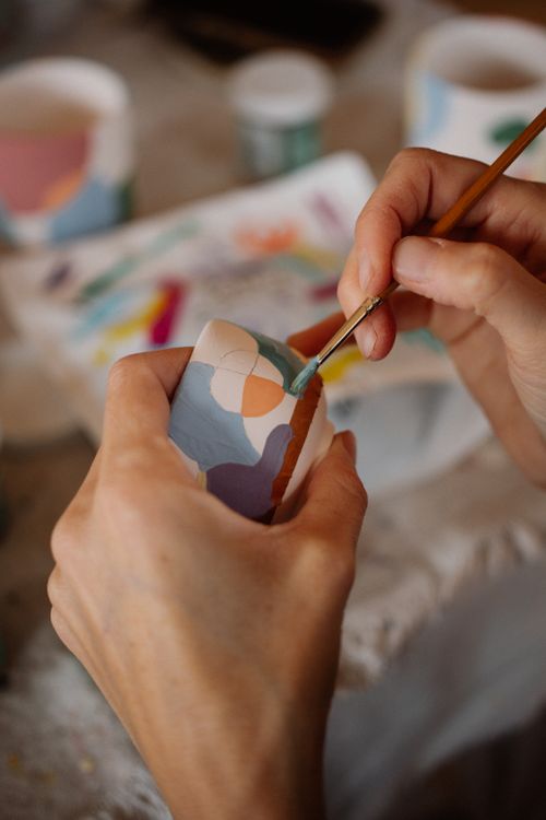 Free Artist hand-painting a colorful ceramic mug with a brush, showcasing creative craftsmanship. Stock Photo