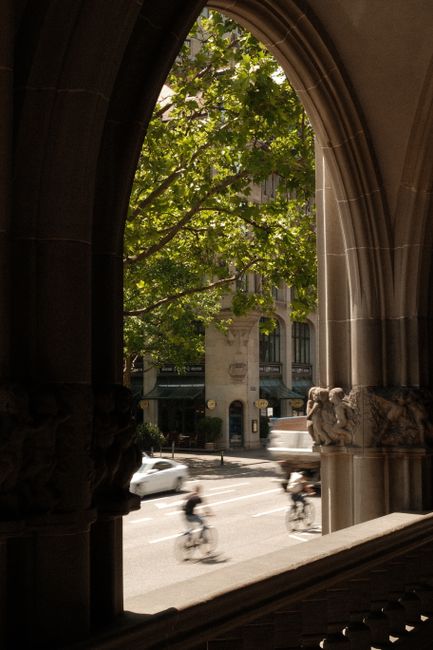 View of Zurich city street captured through a historical archway, with cyclists and greenery.