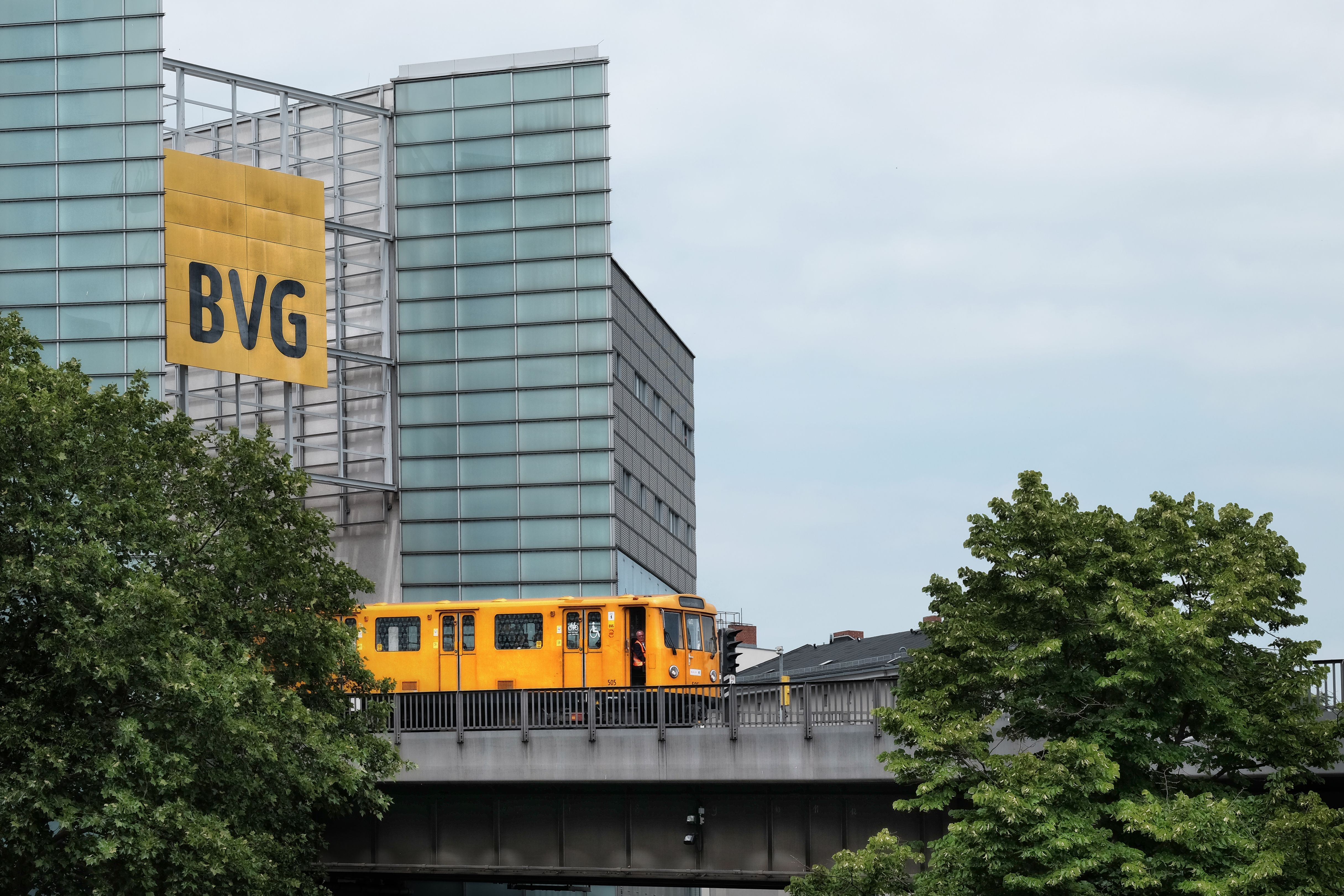 Eine gelbe U-Bahn fährt auf einer Hochbahn vor einer modernen Gebäudefassade.
