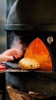 A hand placing freshly baked bread in a traditional wood-fired oven for a perfect crust.