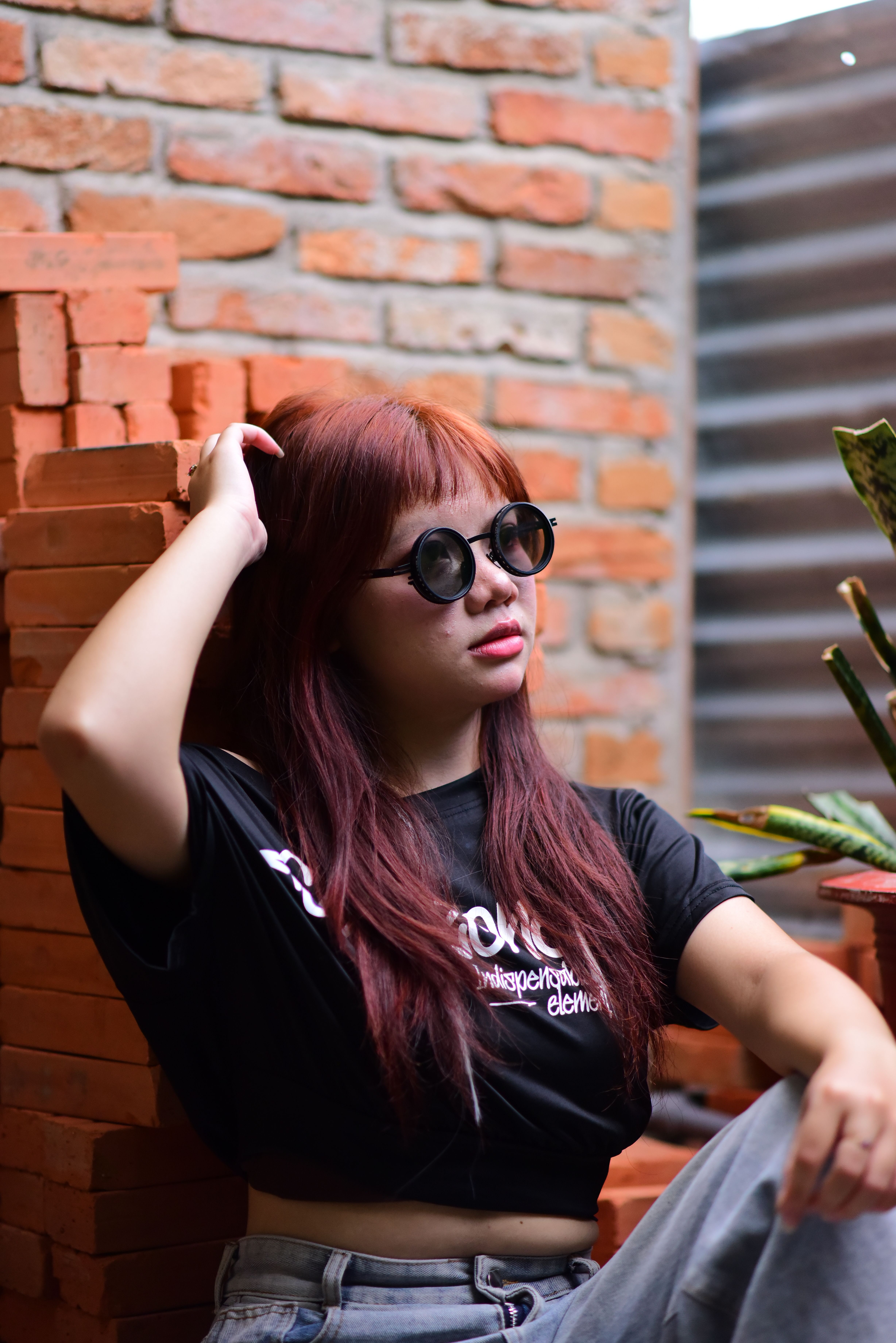 Casual portrait of a young woman with red hair and sunglasses against a brick wall.
