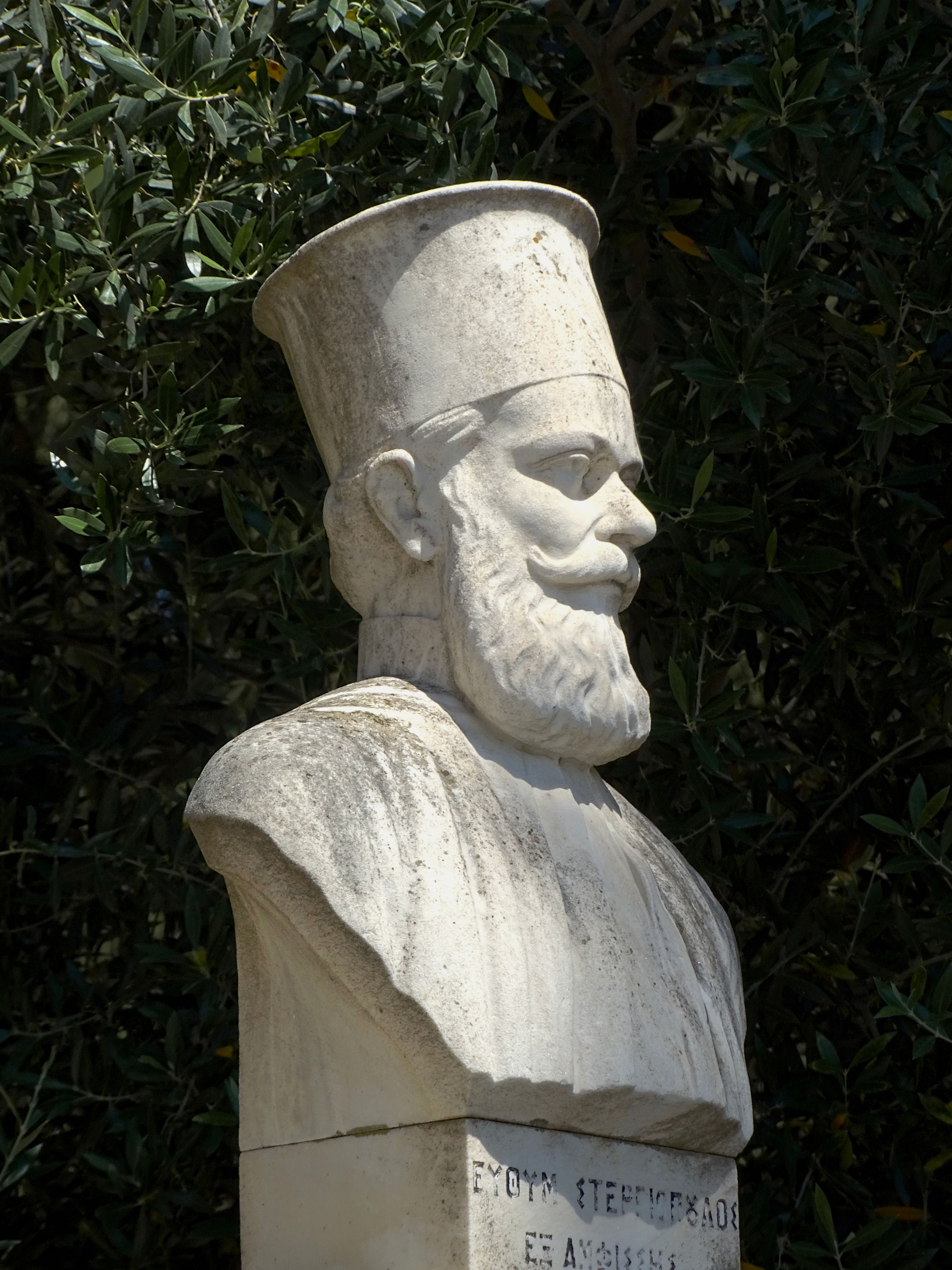 Marble bust of a historic figure set against lush green foliage, outdoor daytime capture.