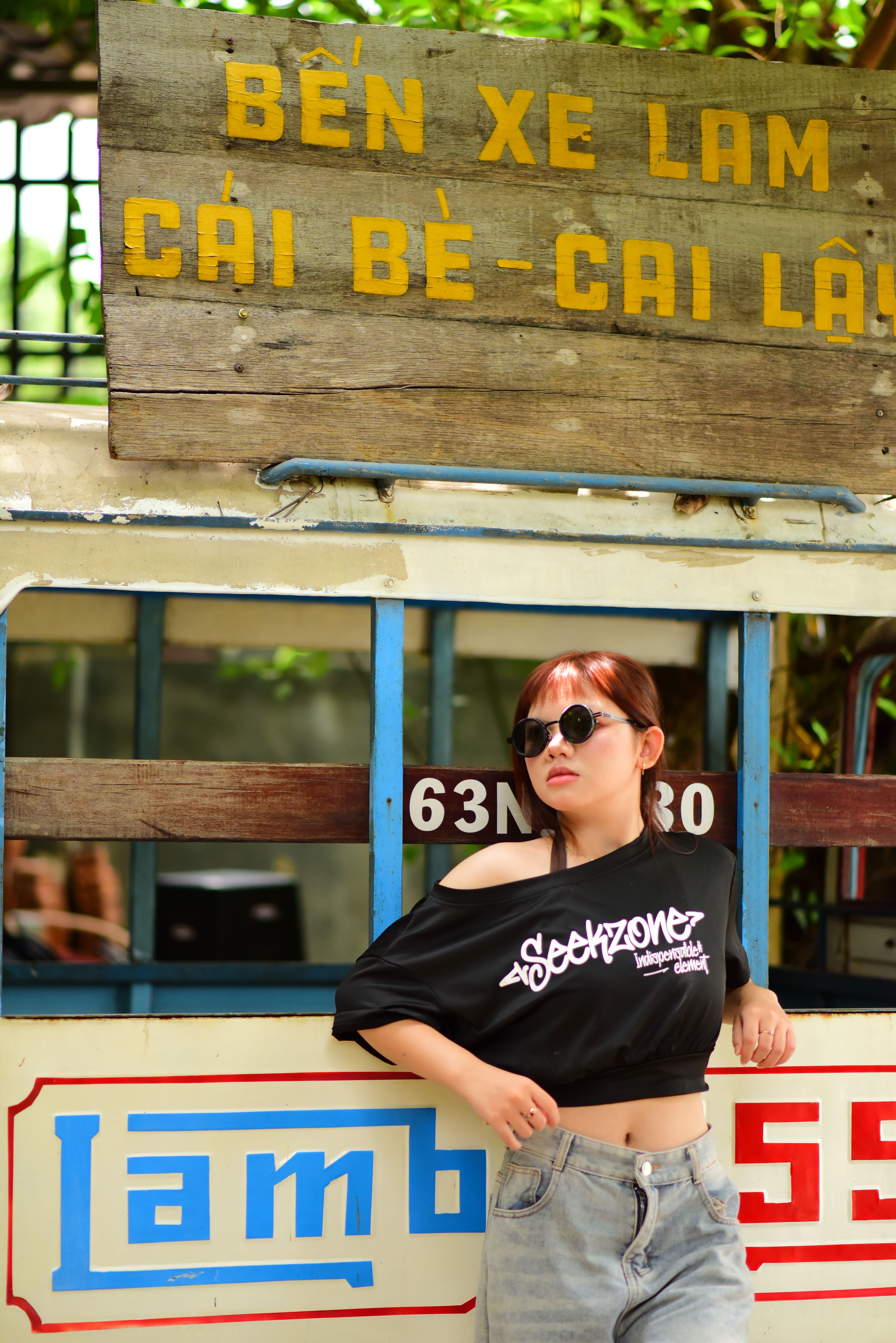 Stylish woman in sunglasses leaning against a vintage vehicle with vibrant signage.