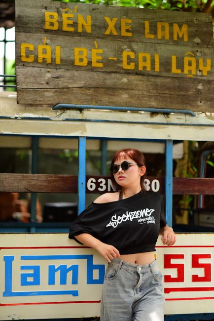 Trendy woman in sunglasses poses by a retro Vietnamese 'Bến Xe Lam' with stylized text.