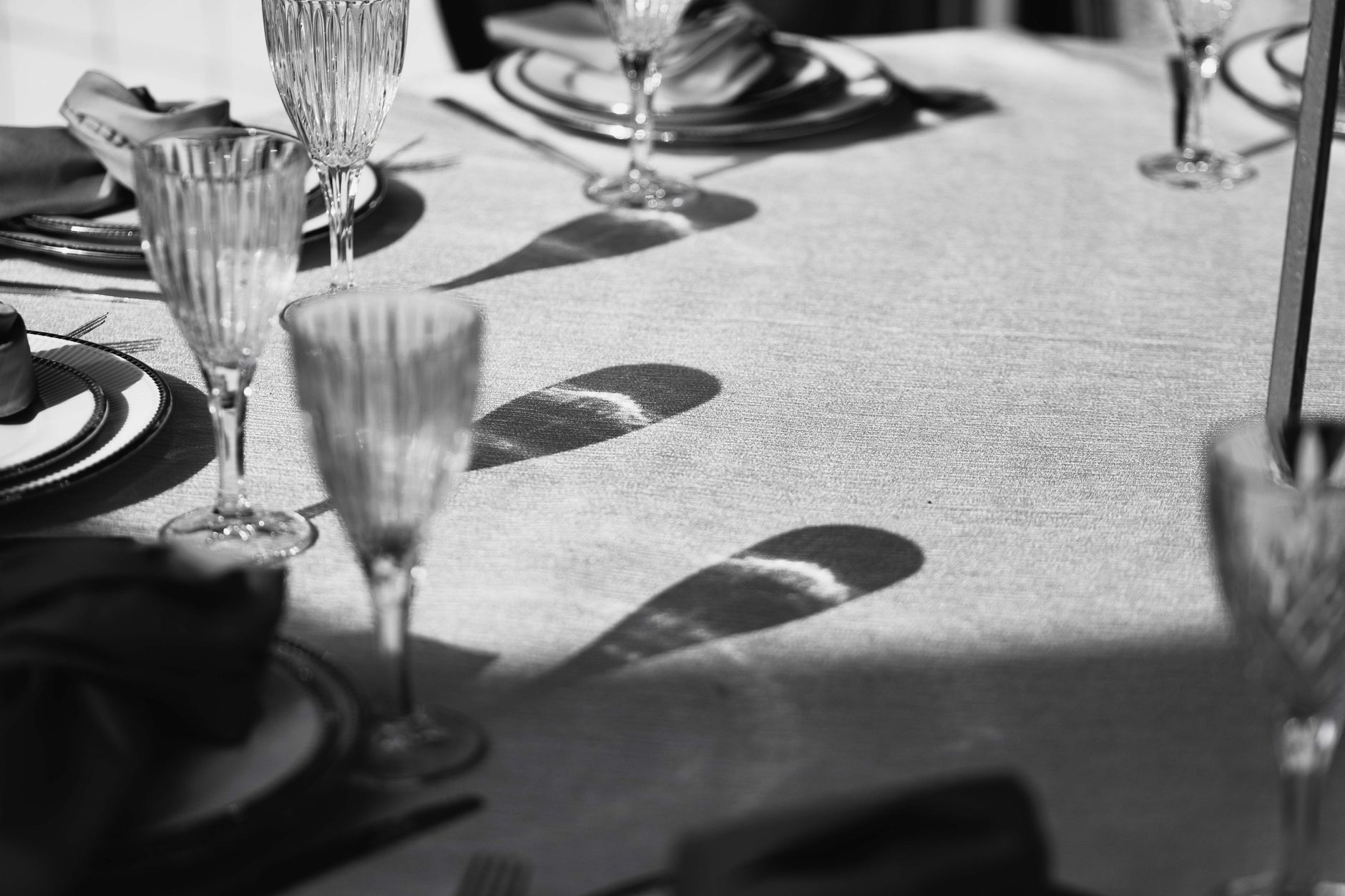 Black and white photo of elegant table setting with glassware casting shadows.