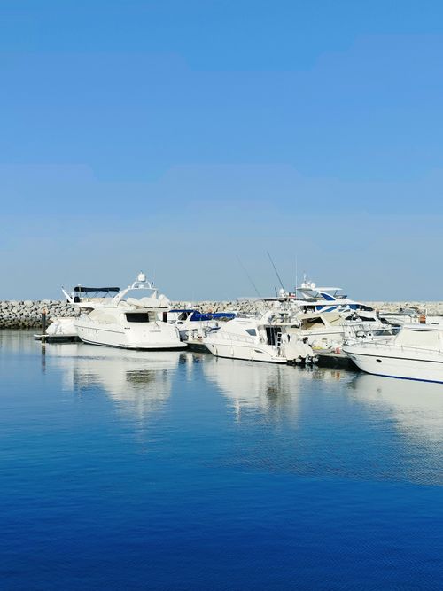 Free A sunny marina scene featuring luxury yachts reflecting on the calm blue water, under a clear sky. Stock Photo