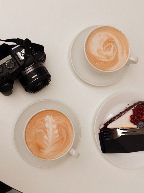 Free Stylish flat lay of cappuccinos and berry cheesecake with a camera on a white table. Stock Photo