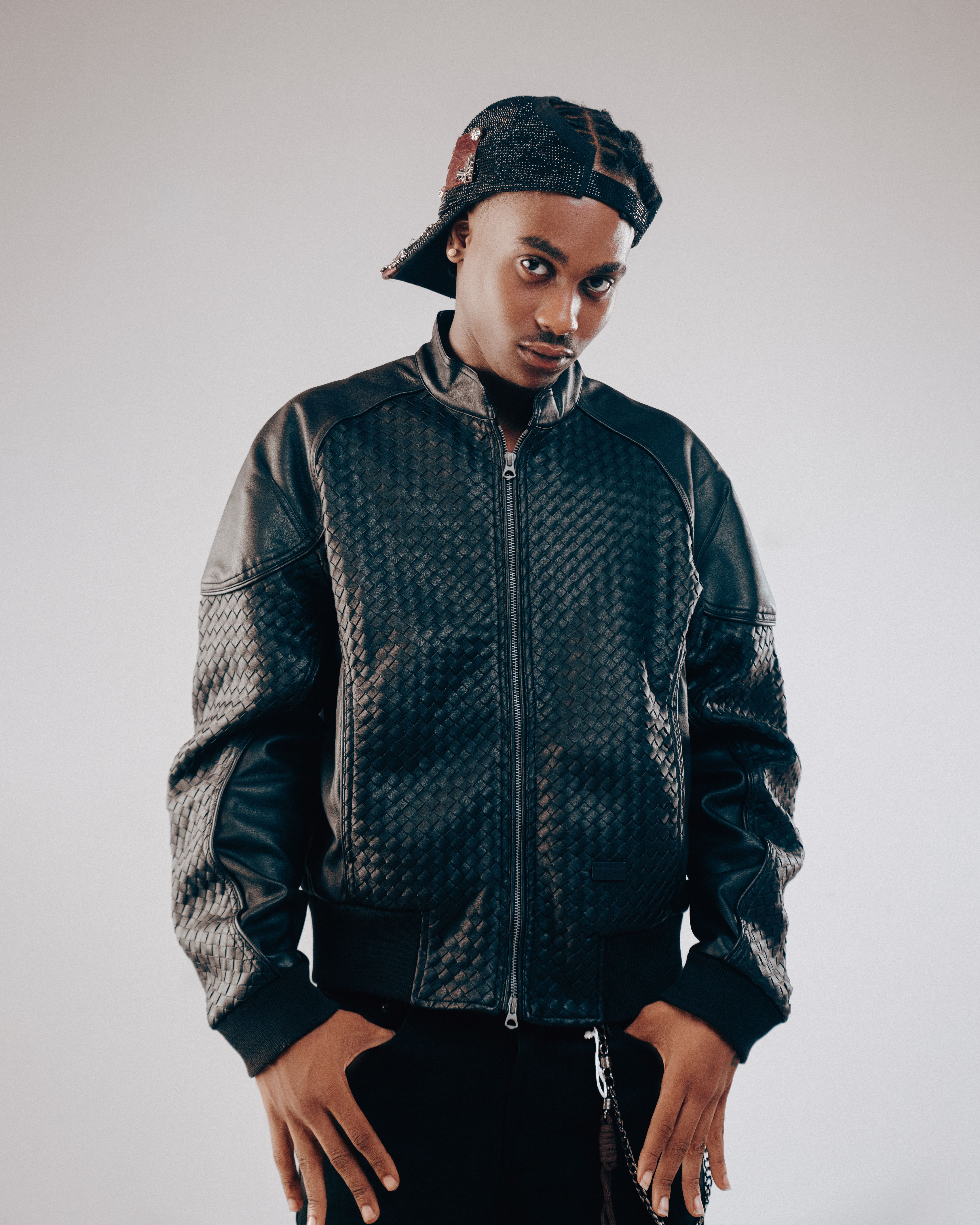 Stylish young man wearing a black leather jacket and cap poses confidently.