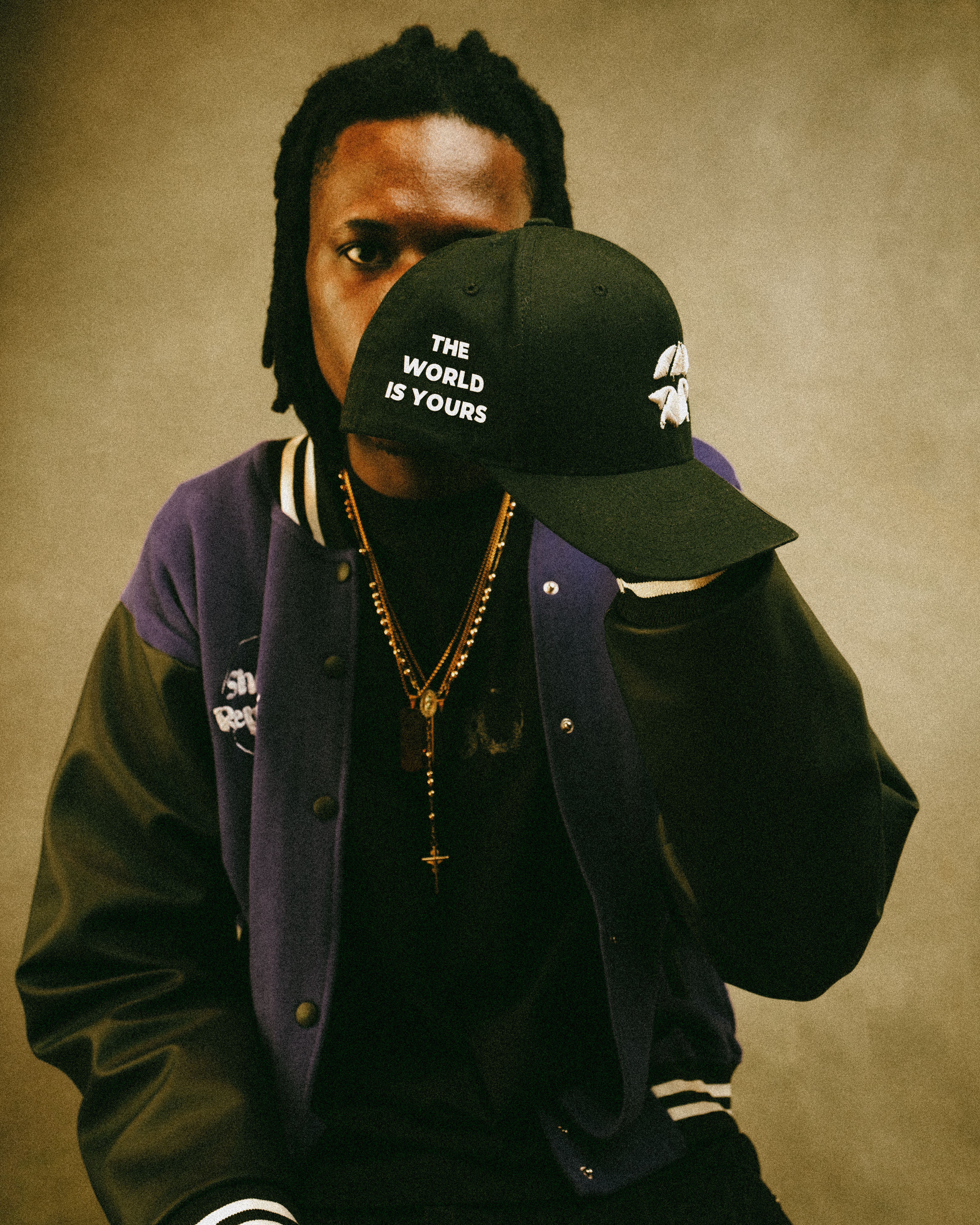 Person holding a cap with 'The World Is Yours' text, exuding confidence.