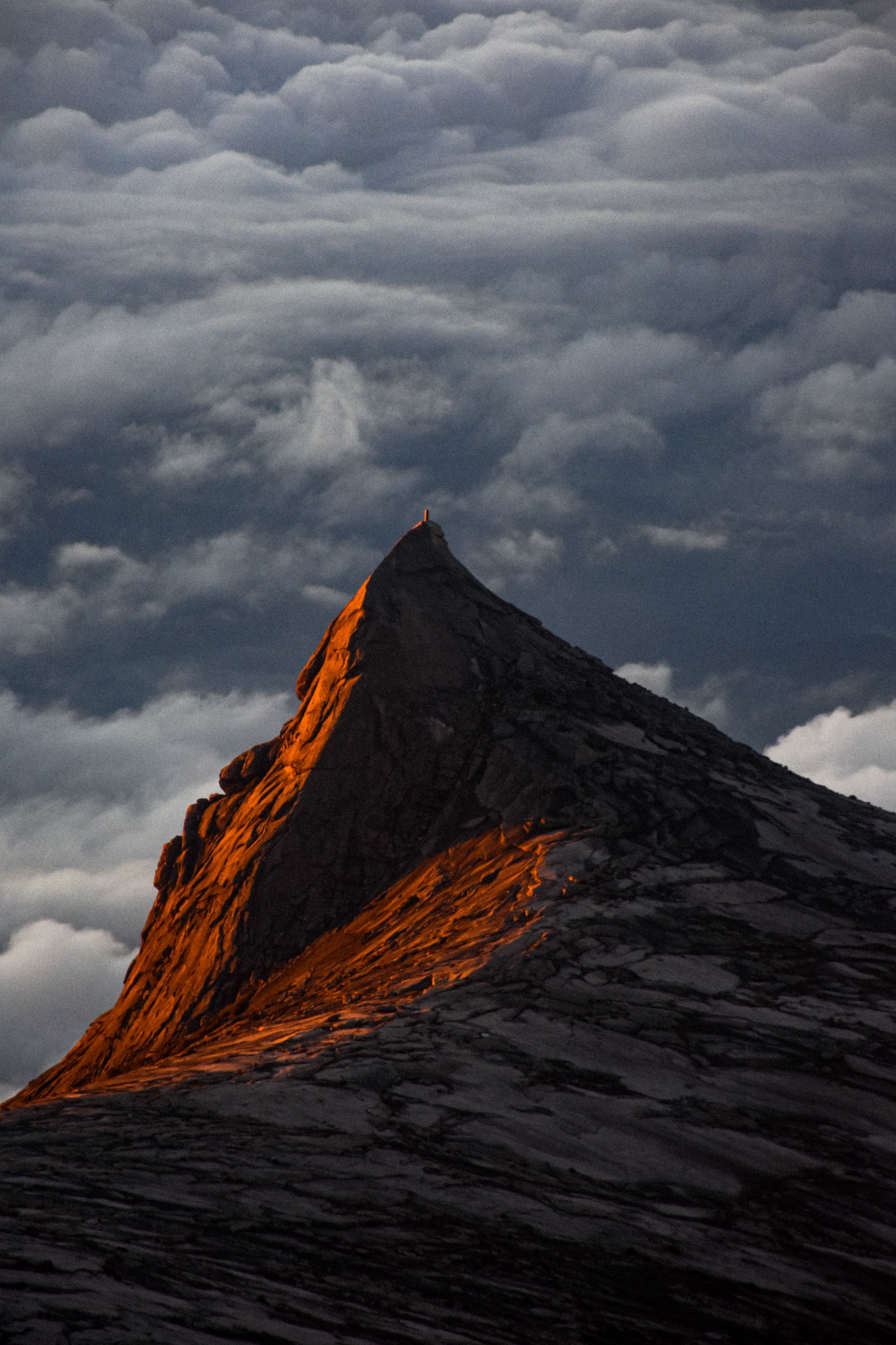 A breathtaking view of Mount Kinabalu at sunset, with golden light illuminating the peak amidst clouds.