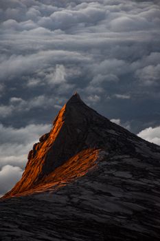 A breathtaking view of Mount Kinabalu at sunset, with golden light illuminating the peak amidst clouds.