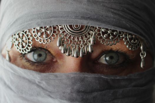 Captivating image of mysterious eyes peering through a veil adorned with ornate jewelry.