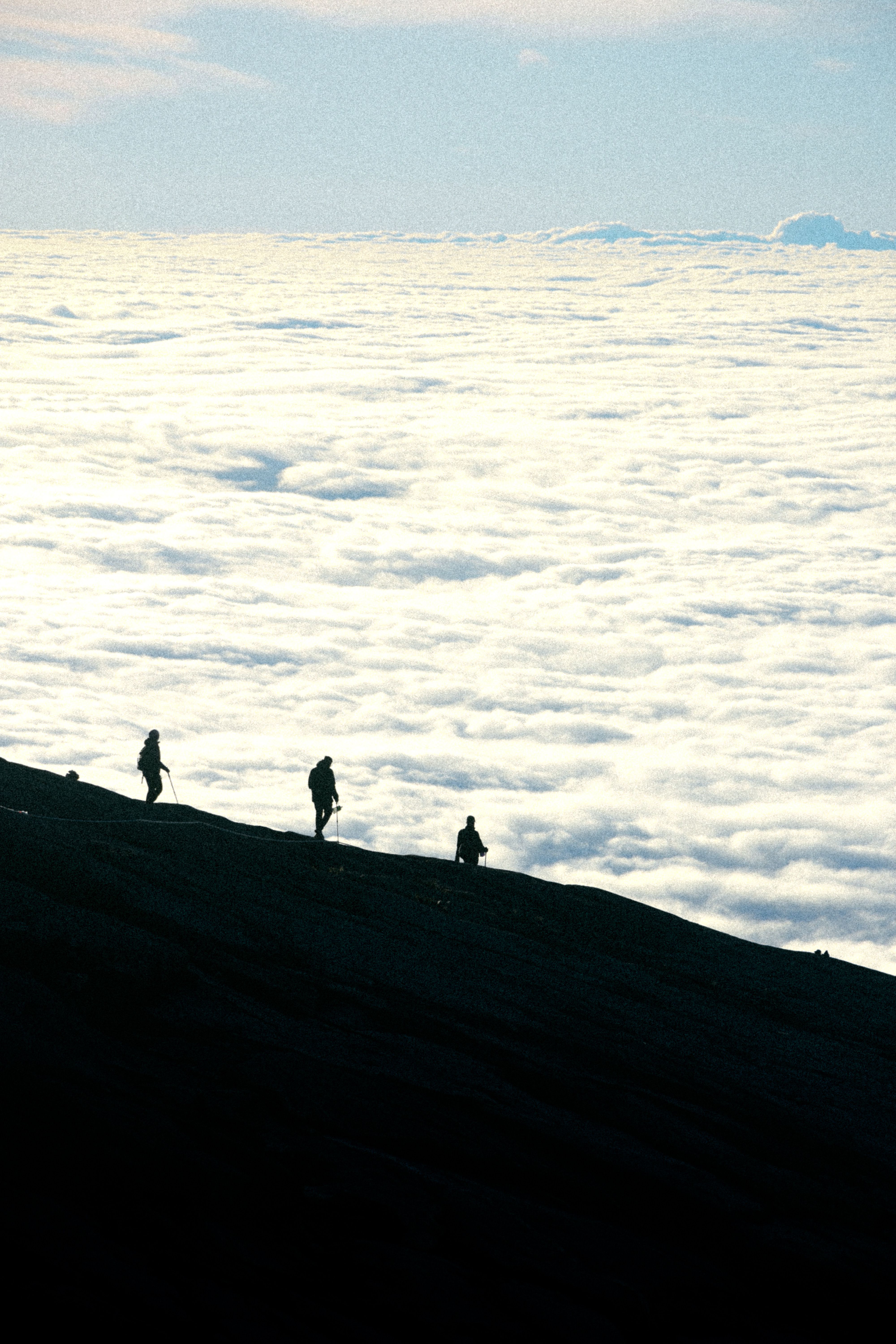 Silhouetted hikers ascend a mist-covered mountain in Kota Kinabalu against a backdrop of clouds.