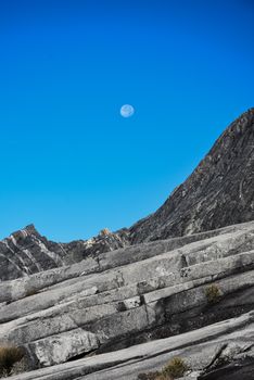 Stunning view of Mount Kinabalu's rocky summit with a clear blue sky and visible moon in Sabah, Malaysia.
