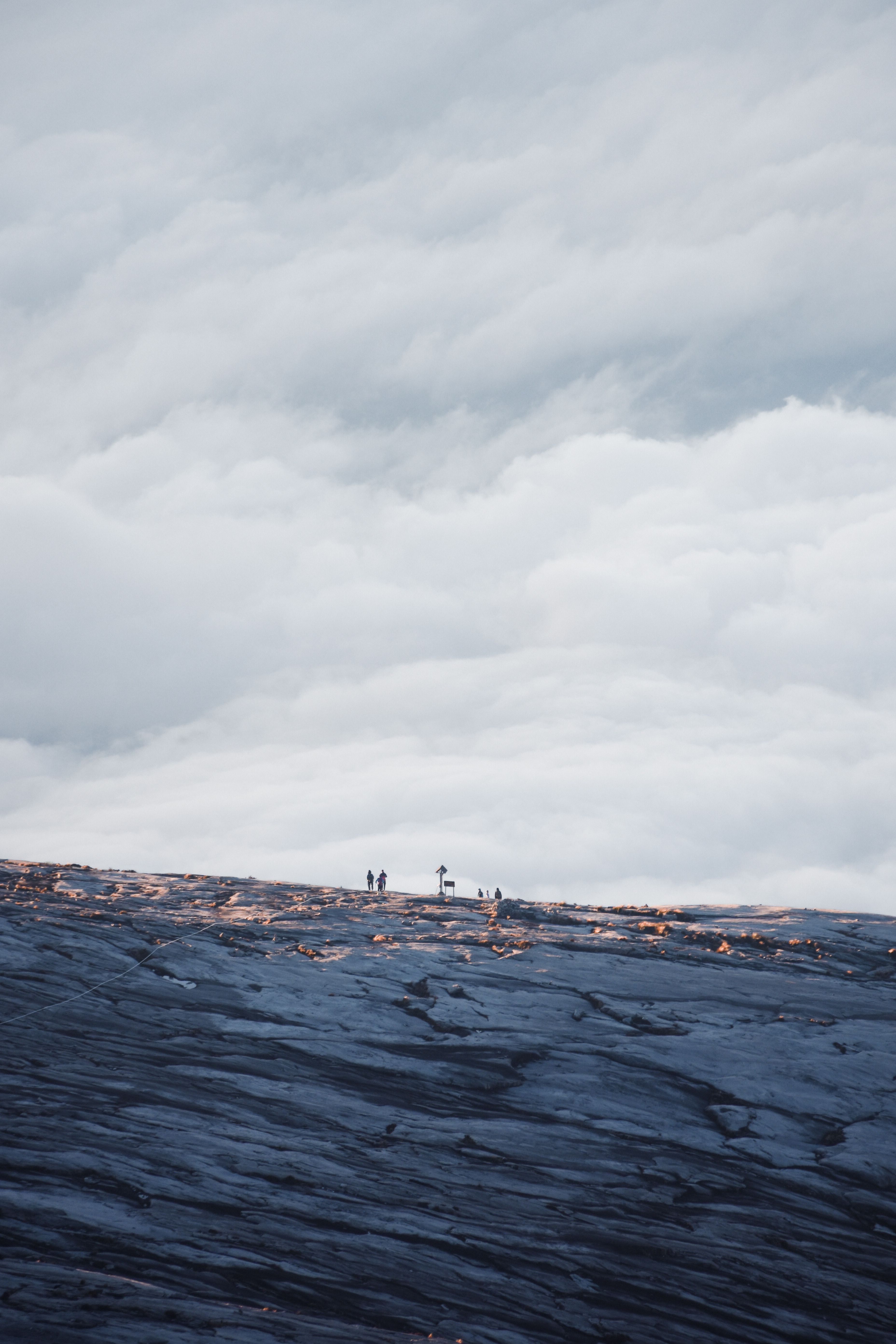 Hikers explore the vast rocky terrain of Mount Kinabalu under a dramatic cloudy sky in Sabah, Malaysia.