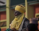 A person in ornate traditional attire with a yellow turban, attending a cultural event outdoors.