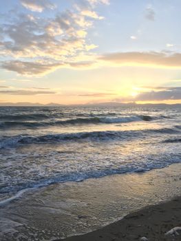 Tranquil ocean sunset with gentle waves lapping the sandy shore under a soft golden sky.