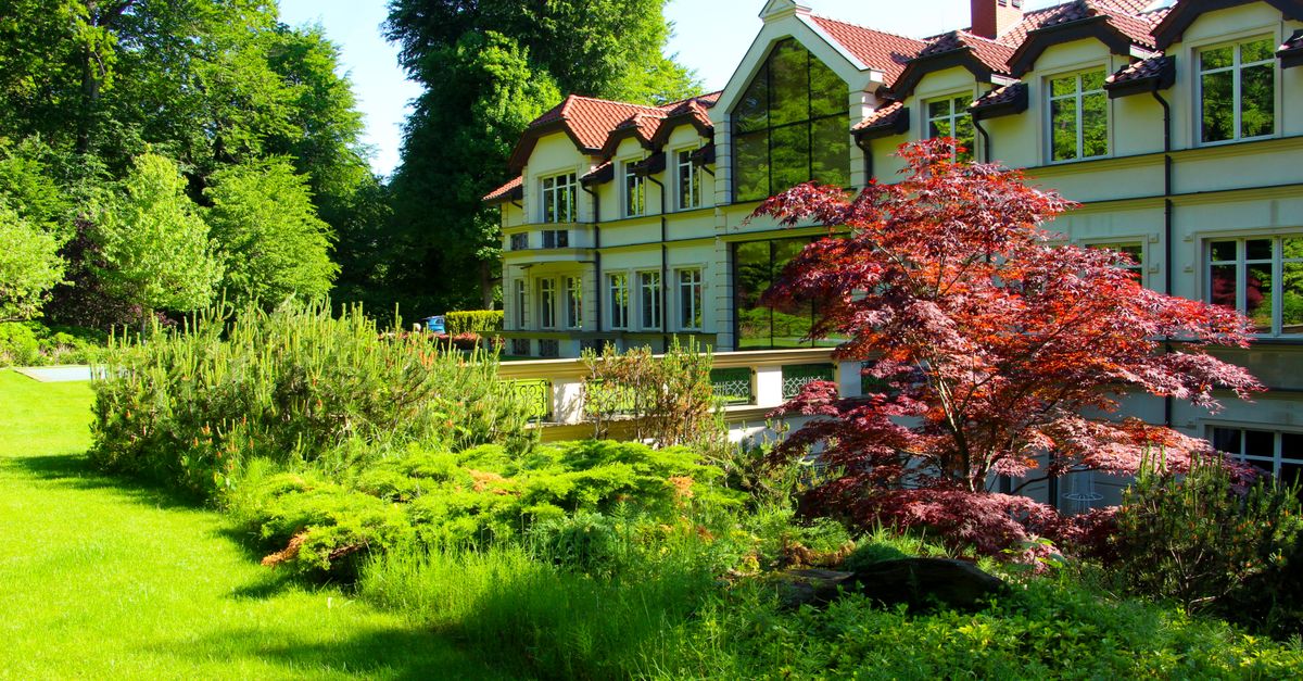 A beautiful European-style house bordered by a vibrant, lush garden under a bright summer day.