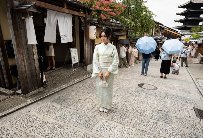 A woman in a kimono stands on a traditional Kyoto street with pagoda in the background.