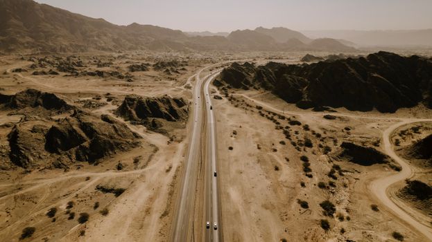 A scenic aerial view of a desert highway snaking through rocky landscapes in Oman.