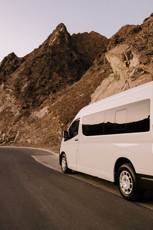 Free A white van travels a picturesque mountain road at sunset, showcasing Oman's rugged landscape. Stock Photo