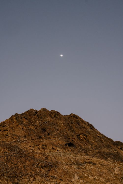 Free An enchanting view of the moon above a rugged rocky hill in Oman under a clear night sky. Stock Photo