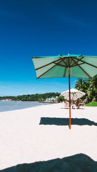 A sunny tropical beach featuring a green beach umbrella, clear blue sky, and distant trees.
