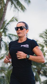 Athletic woman jogging outdoors with palm trees, showcasing fitness lifestyle.