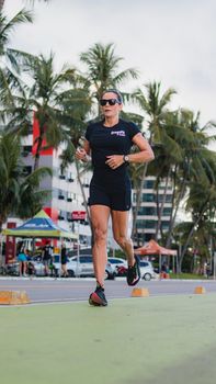 Female runner exercising outdoors in a vibrant tropical urban setting with palm trees.