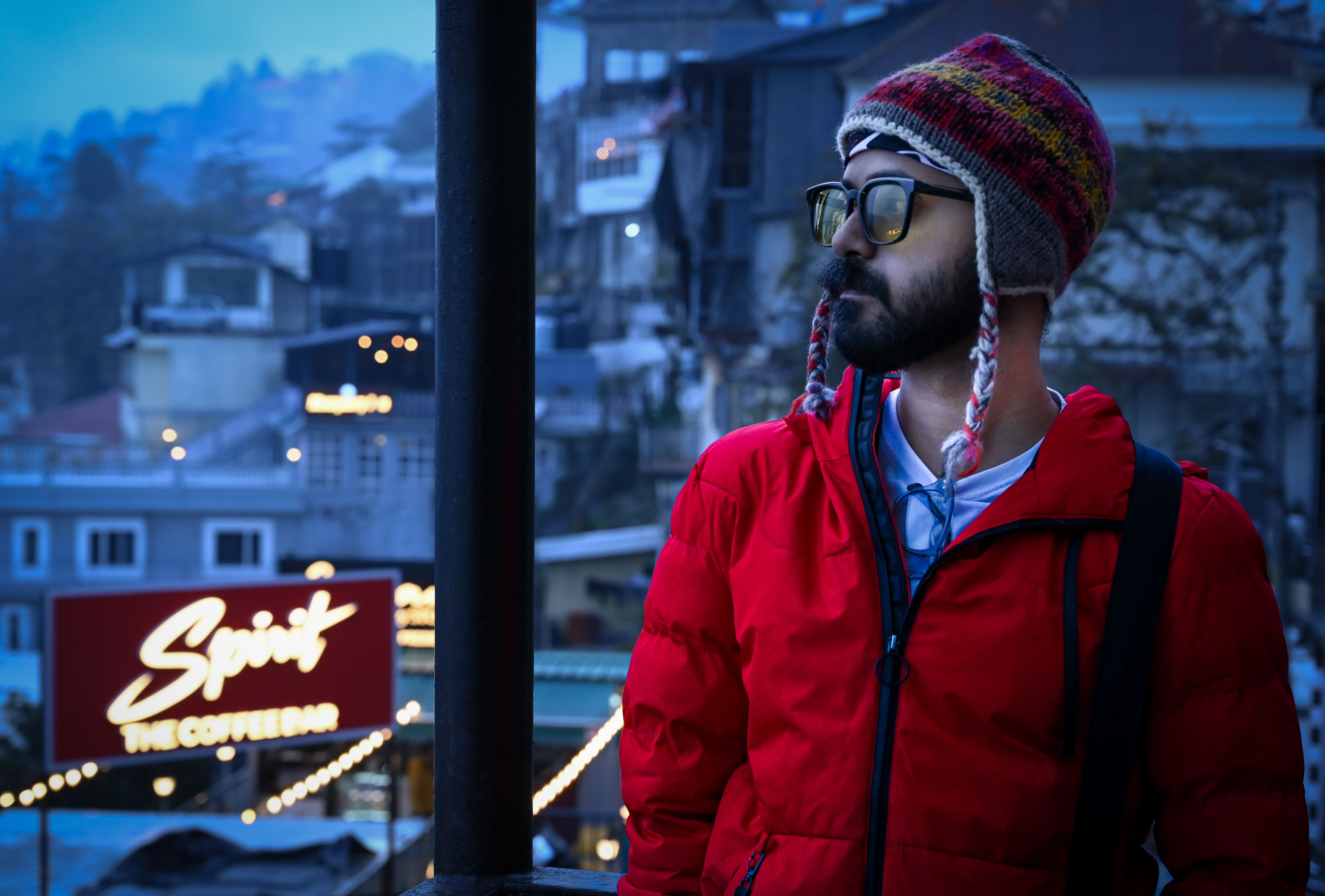 [ColoSach]-man-with-beanie-in-vibrant-red-jacket-at-twilight-near-lit-coffee-bar-in-urban-setting.