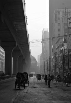 Monochrome urban street with rickshaws and elevated track in the morning light.