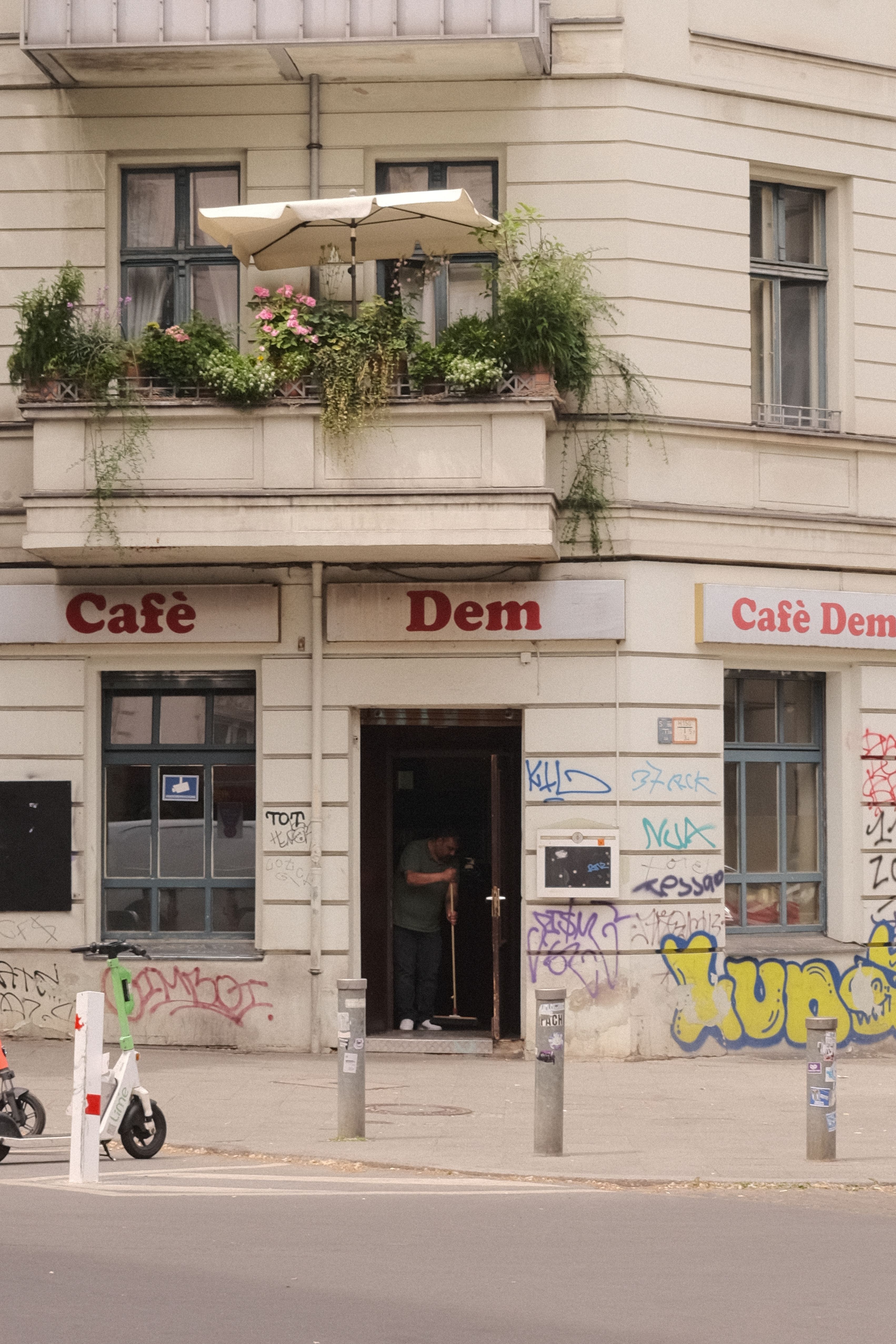 Urban street scene featuring Café Dem in Berlin, with vibrant graffiti and lush balcony plants.