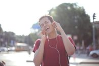 Delighted African American young male in casual wear enjoying songs in earphones on street and singing along loudly while standing in city with closed eyes