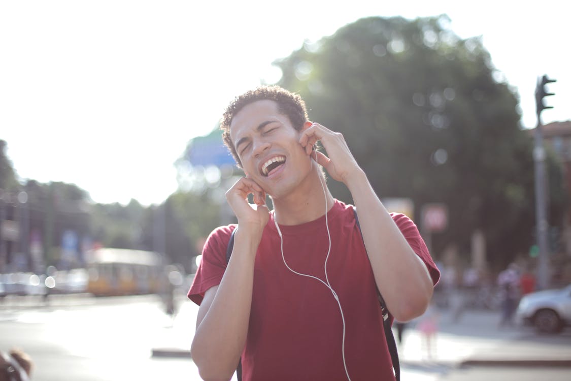 Free Delighted African American young male in casual wear enjoying songs in earphones on street and singing along loudly while standing in city with closed eyes Stock Photo