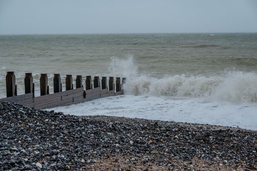 Free Waves crashing on a rocky shoreline with wooden breakwater under an overcast sky. Stock Photo