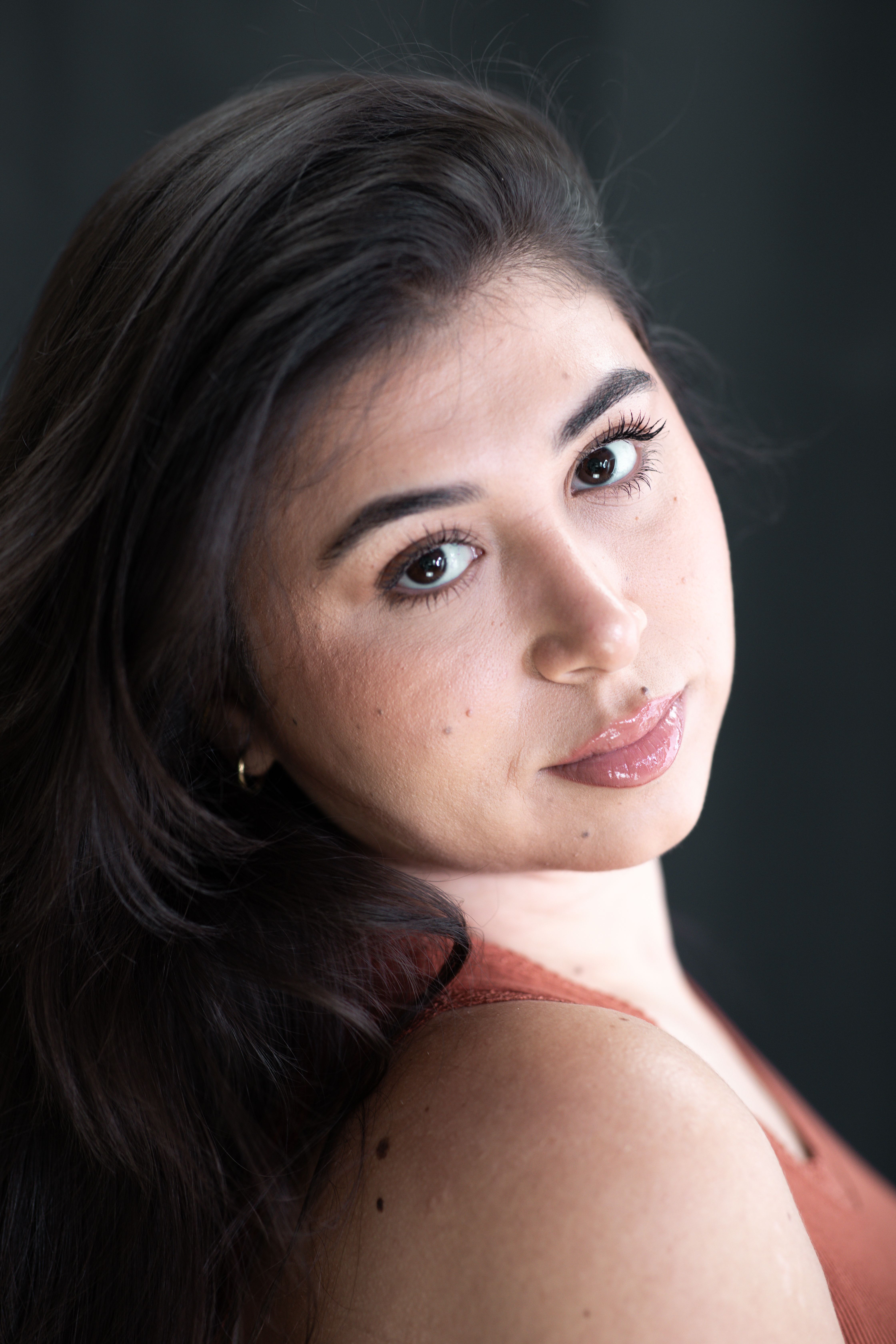 Close-up portrait of a young woman with long dark hair, looking over shoulder.