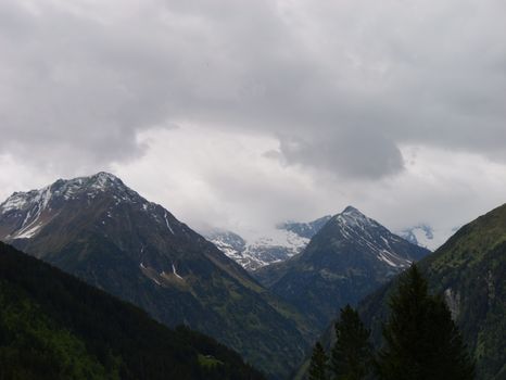 Snow-capped alpine mountains under a dramatic cloudy sky, showcasing the beauty and serenity of nature.