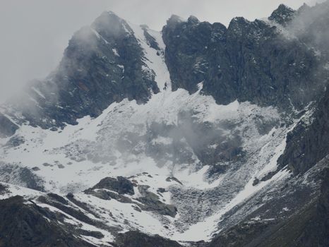 Majestic snow-covered mountain peaks with misty clouds on a winter day.