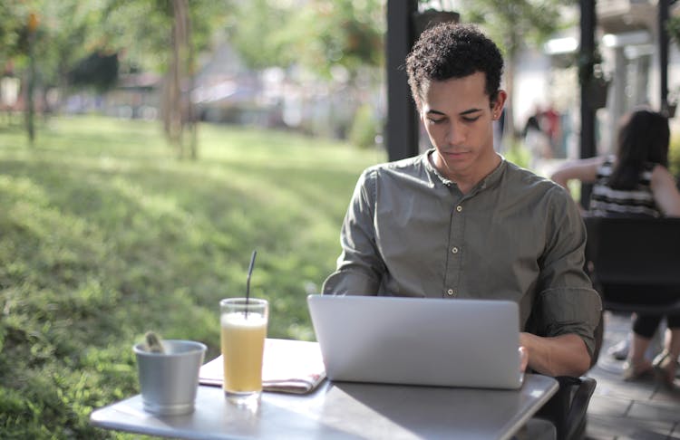 Focused Black Male Freelancer Using Laptop In Street Cafe