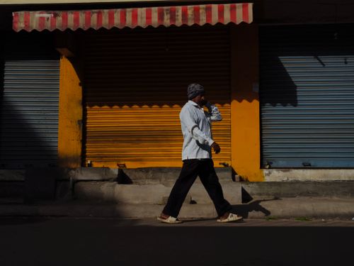 Free A man walks in front of closed colored shop shutters in bright sunlight, creating contrast. Stock Photo